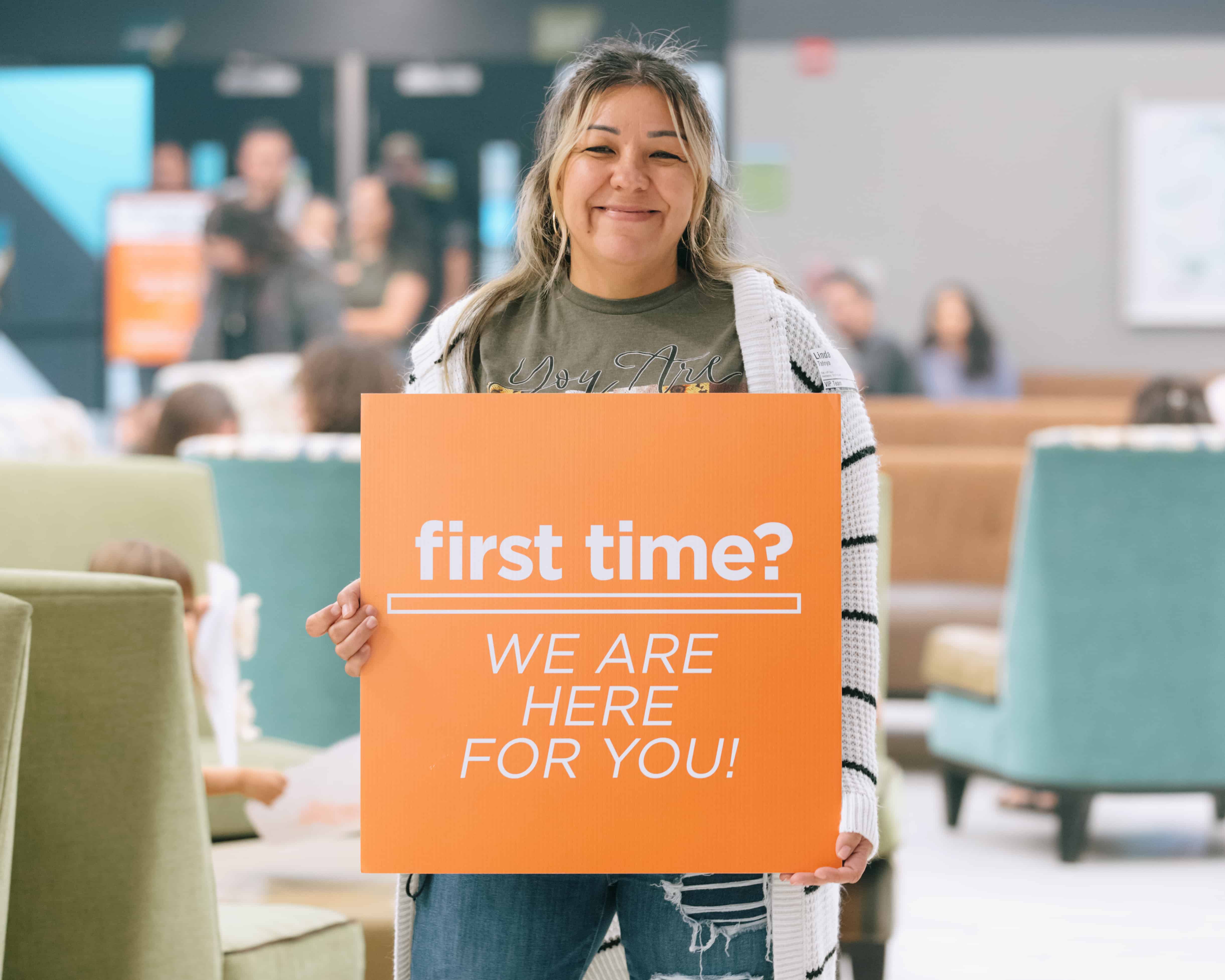 Smiling woman holding "first time?"poster